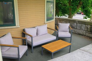 Ein überdachter Patio-Bereich mit einer Couch, zwei Stühlen und einem kleinen Tisch.