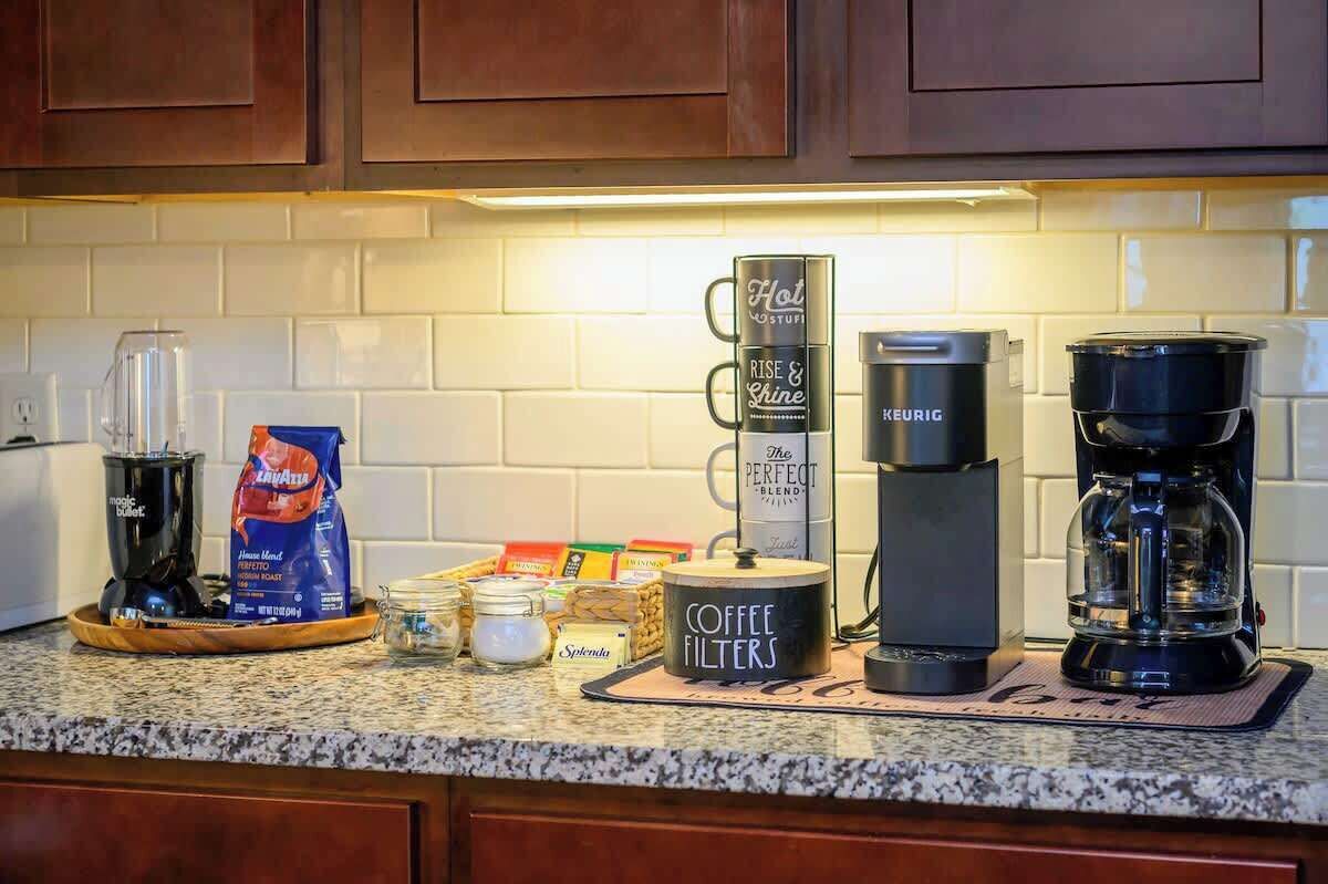 Uma bancada de cozinha com equipamentos para fazer café, incluindo um Keurig, um recipiente para filtro de café e uma cafeteira.