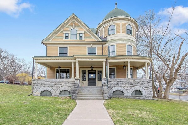 Une maison à deux étages dotée d’une véranda qui fait le tour de la maison et d’une tourelle.