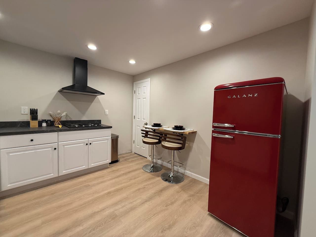 Une cuisine moderne avec des meubles blancs, un réfrigérateur rouge et deux tabourets de bar.