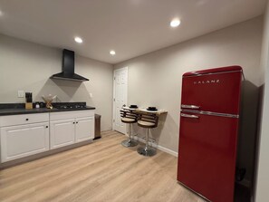 A modern kitchen with white cabinets, a red refrigerator, and two bar stools.