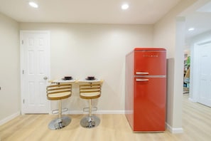 Una cocina compacta con un refrigerador rojo, dos taburetes de madera y una puerta blanca.