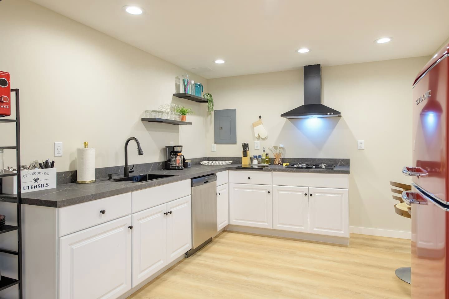 A modern kitchen with white cabinets, a black countertop, a built-in dishwasher, and a red refrigerator.
