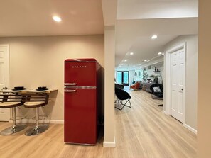 A modern kitchen with a red refrigerator, wooden bar stools, and a dining table.