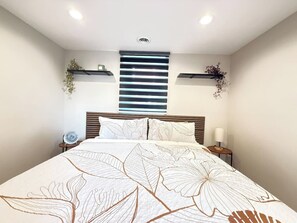 A bedroom with a large bed, bedside tables, a wall-mounted shelf with plants, and a ceiling light.