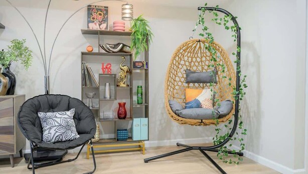 A modern living room with a black chair, a wicker swing chair, and a bookshelf.