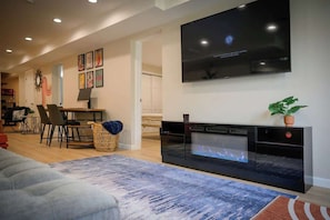Una sala de estar moderna con un televisor de pantalla plana montado en la pared, una chimenea y un comedor con sillas y una mesa.