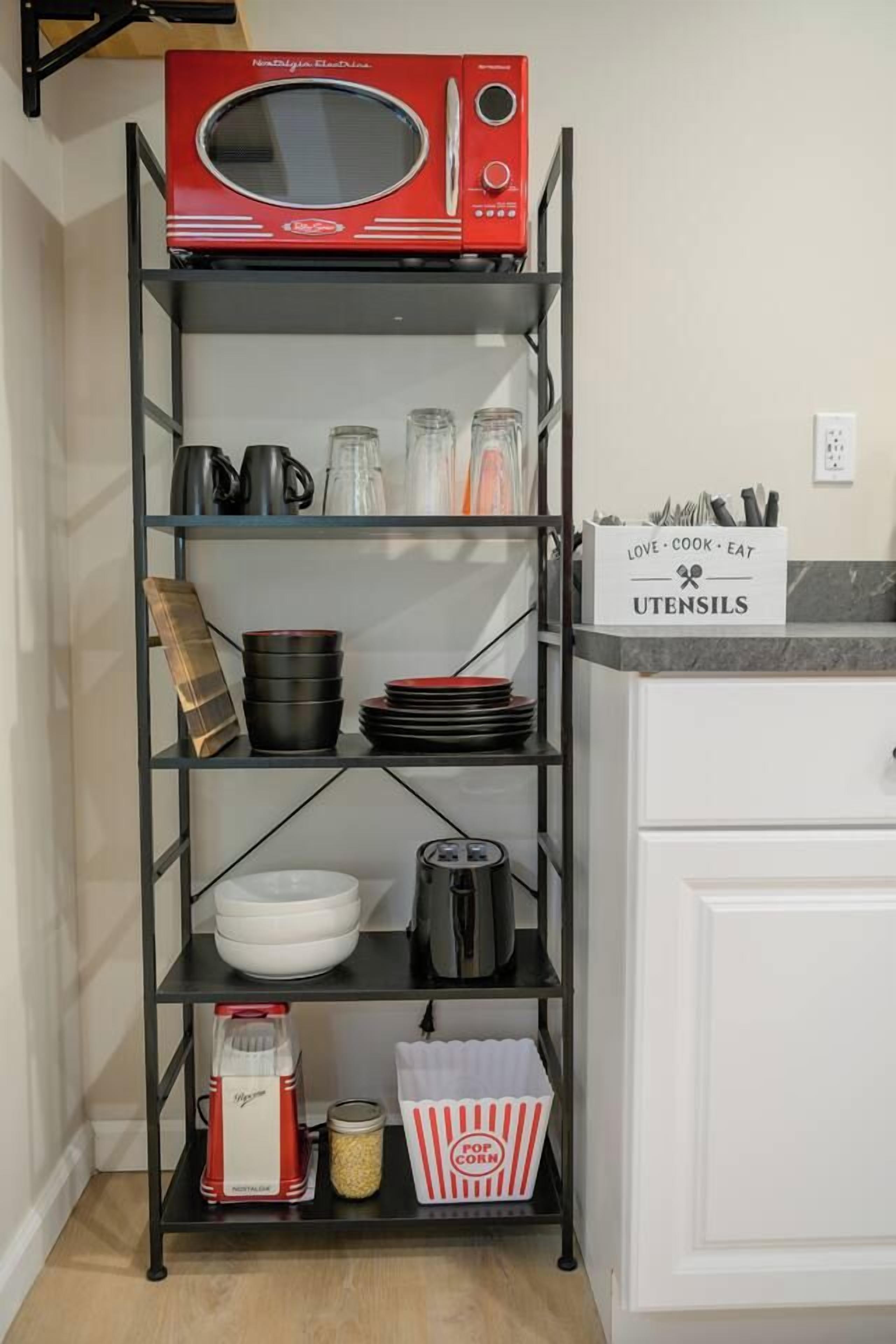A kitchen with a red microwave on a shelf, various kitchen utensils, and a sign labeled 'UTENSILS'.