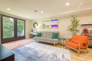 A modern living room with a sofa, armchair, and a coffee table. There is a sliding glass door leading to a balcony.