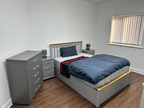 A bedroom with a bed, a dresser, a nightstand, and a window with blinds. - Two bed flat in Manchester—Walk to Uni & Hospitals (Manchester)