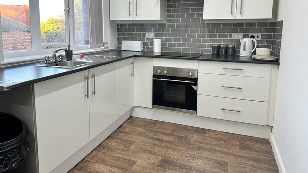 A modern kitchen with white cabinets, a black countertop, and a window with a view of a brick building. - Two bed flat in Manchester—Walk to Uni & Hospitals (Manchester)