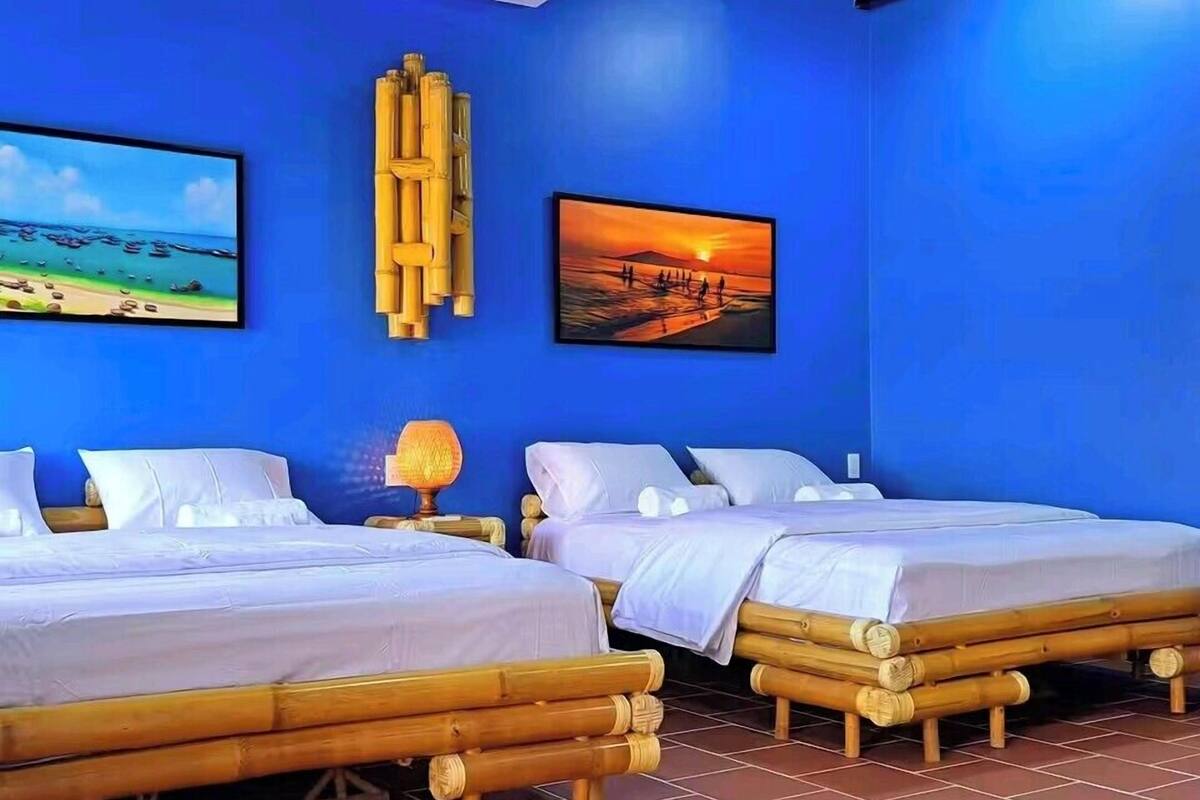 A room with two beds, a blue wall, and two framed pictures.