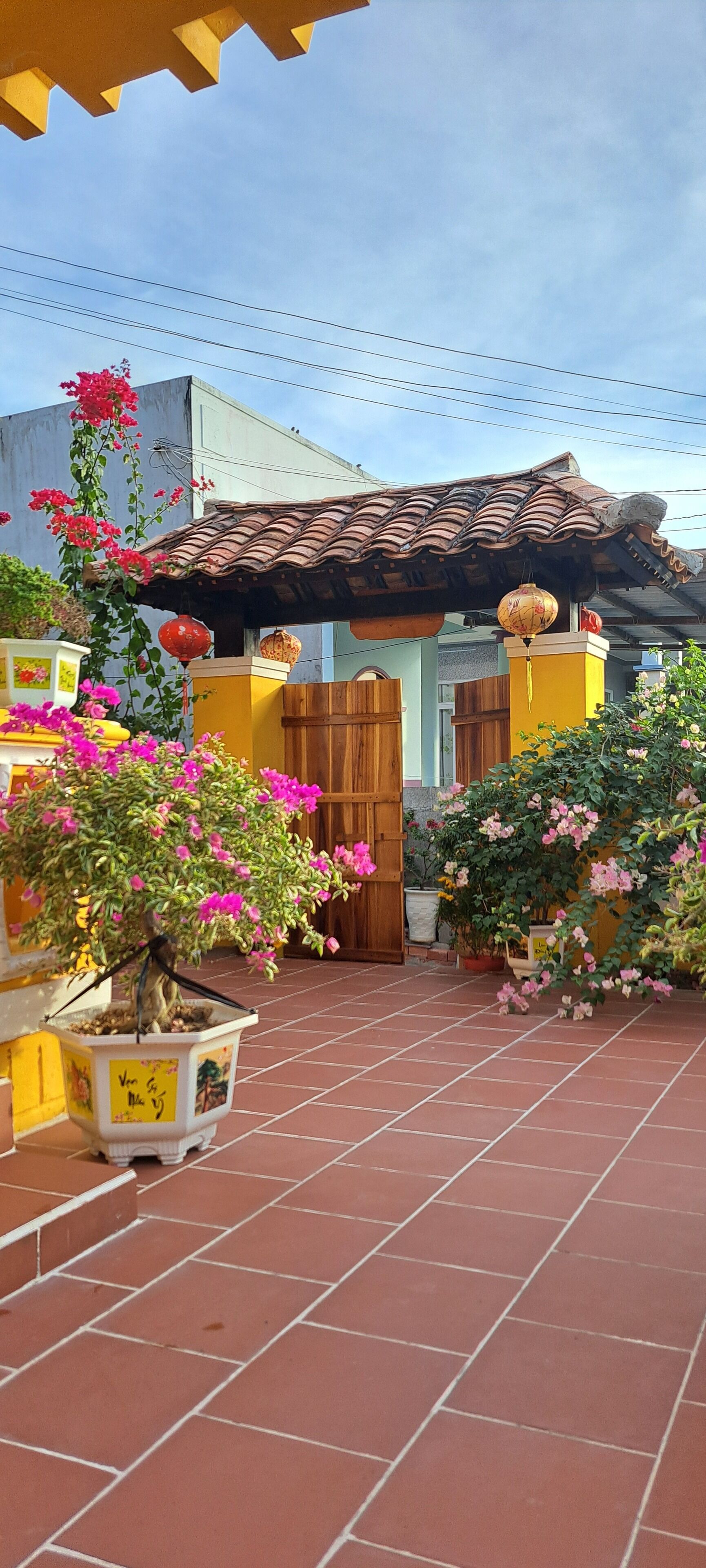 Un patio con suelo de baldosas, una puerta de madera y macetas con flores rosadas.
