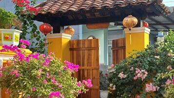 Un patio con suelo de baldosas, una puerta de madera y macetas con flores rosadas.