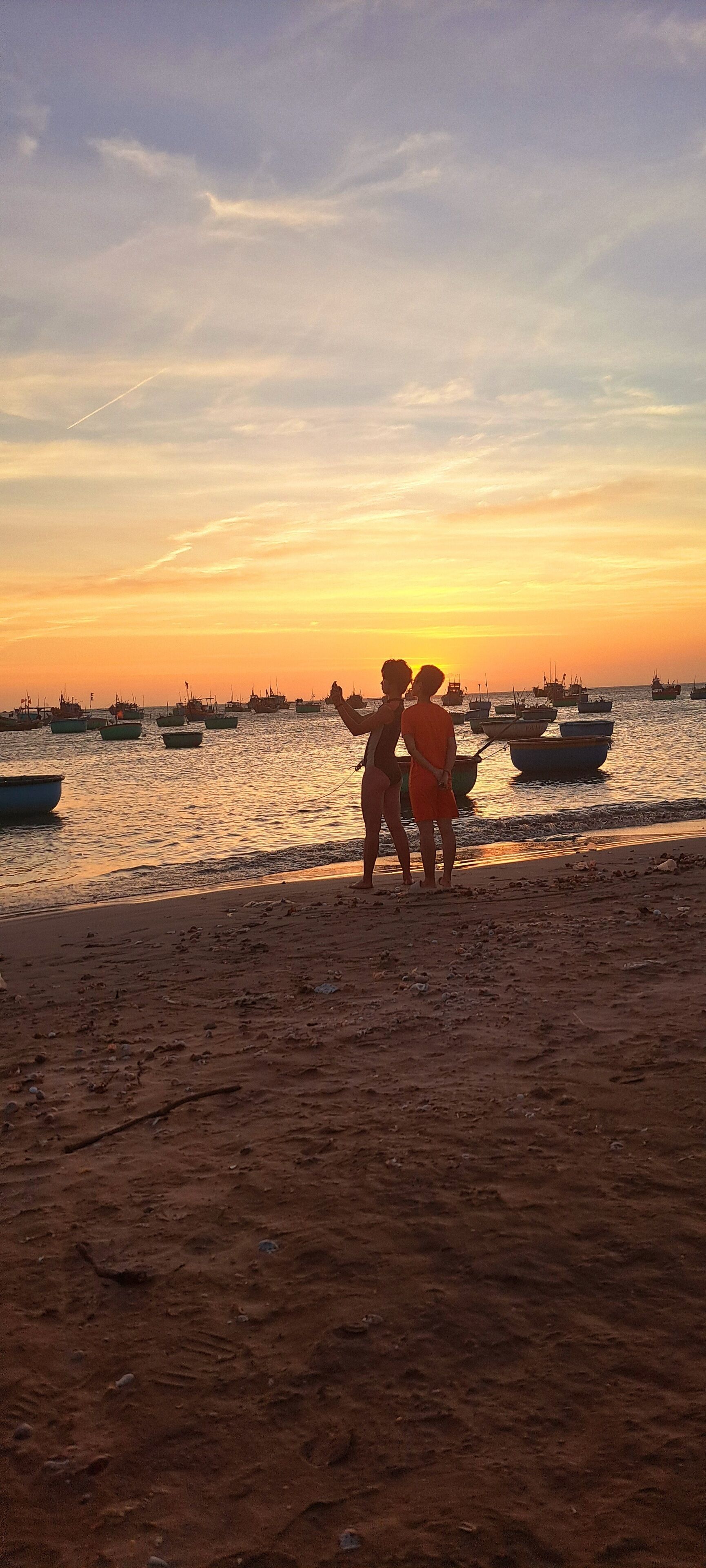 Una spiaggia con barche in acqua e due persone in piedi sulla sabbia.
