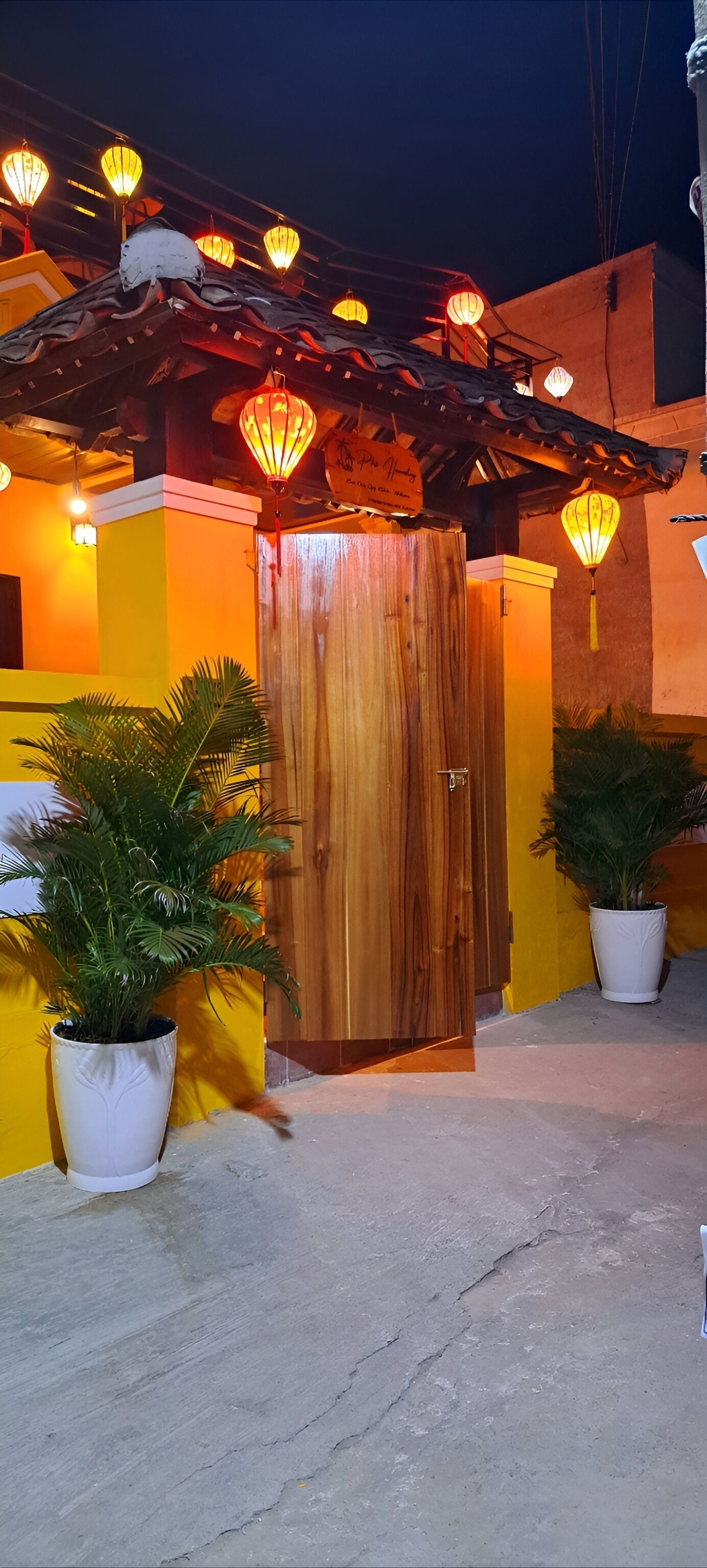 Une entrée d’immeuble avec une porte en bois, des plantes en pot et des lanternes suspendues.