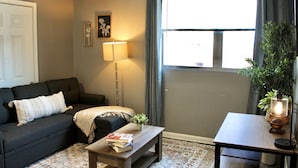 A living room with a sofa, a coffee table with books, a floor lamp, and a potted plant. - Modern Hideaway: Steps from Sights & City Vibes (Little Rock)