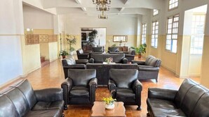 A spacious lobby with leather sofas arranged in a U-shape around a central wooden coffee table, a chandelier hanging from the ceiling, and large windows allowing natural light. - Cozy apartment in the Imperial Condominium (Lambari)