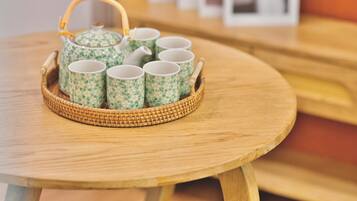 A round wooden table with a woven basket containing a teapot and six cups with floral patterns.