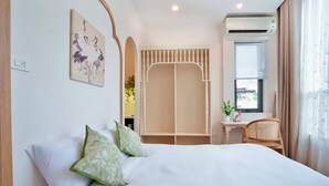 Un dormitorio con cama, almohadas, un escritorio, una silla, aire acondicionado y una ventana con cortinas.