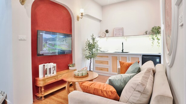 Una sala de estar con una pared de acento roja, un televisor de pantalla plana, una mesa de centro de madera y un sofá color beige.