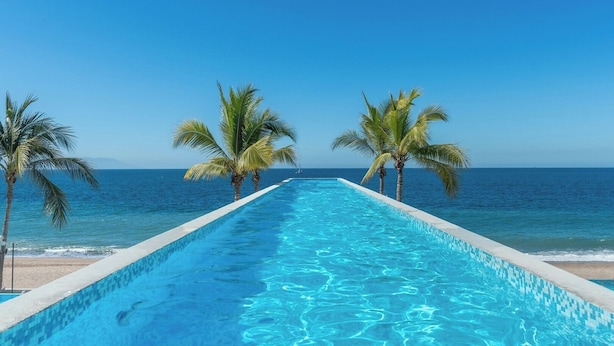 En lang swimmingpool med krystalklart blåt vand, omkranset af palmer, der fører ud til havet.