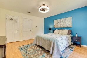 Un dormitorio con cama, mesita de noche, lámpara, ventilador de techo y un cuadro en la pared.