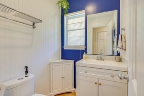 Un baño con inodoro, lavamanos con espejo y ventana con persianas.