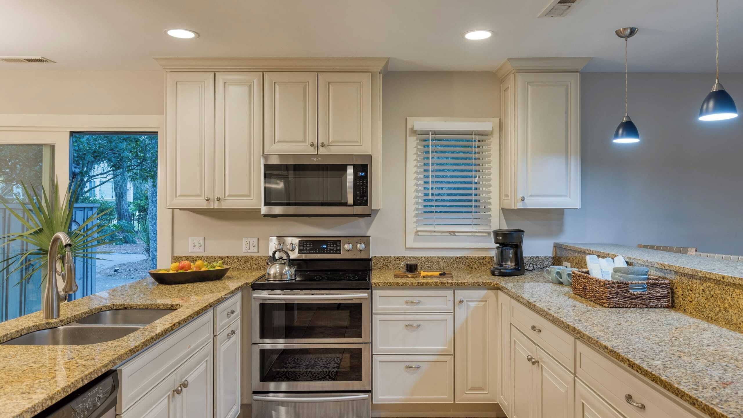 A modern kitchen with white cabinetry, stainless steel appliances, granite countertops, and a view of the outdoors.