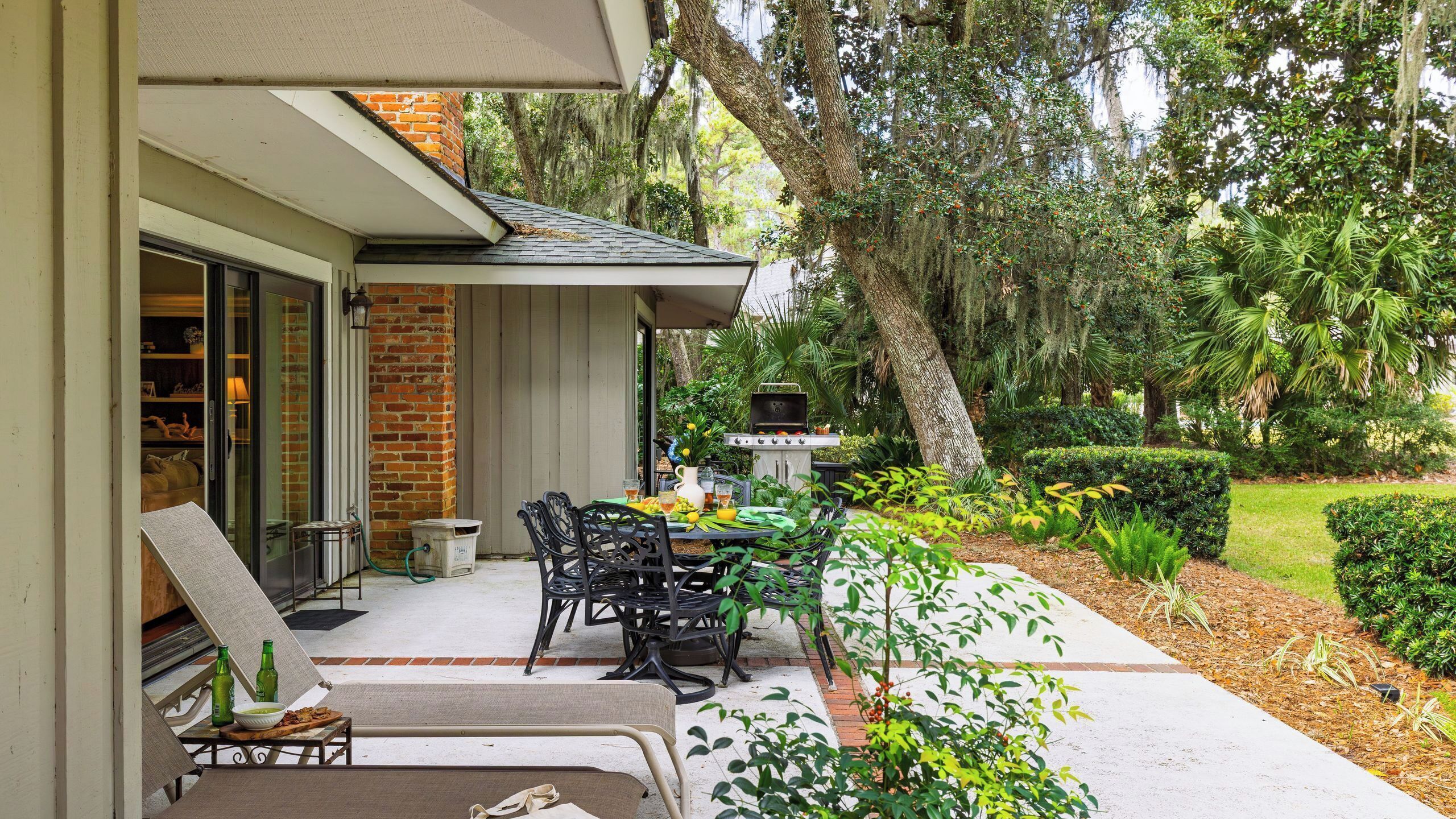 An outdoor patio with a table and chairs, a grill, and a garden with various plants.