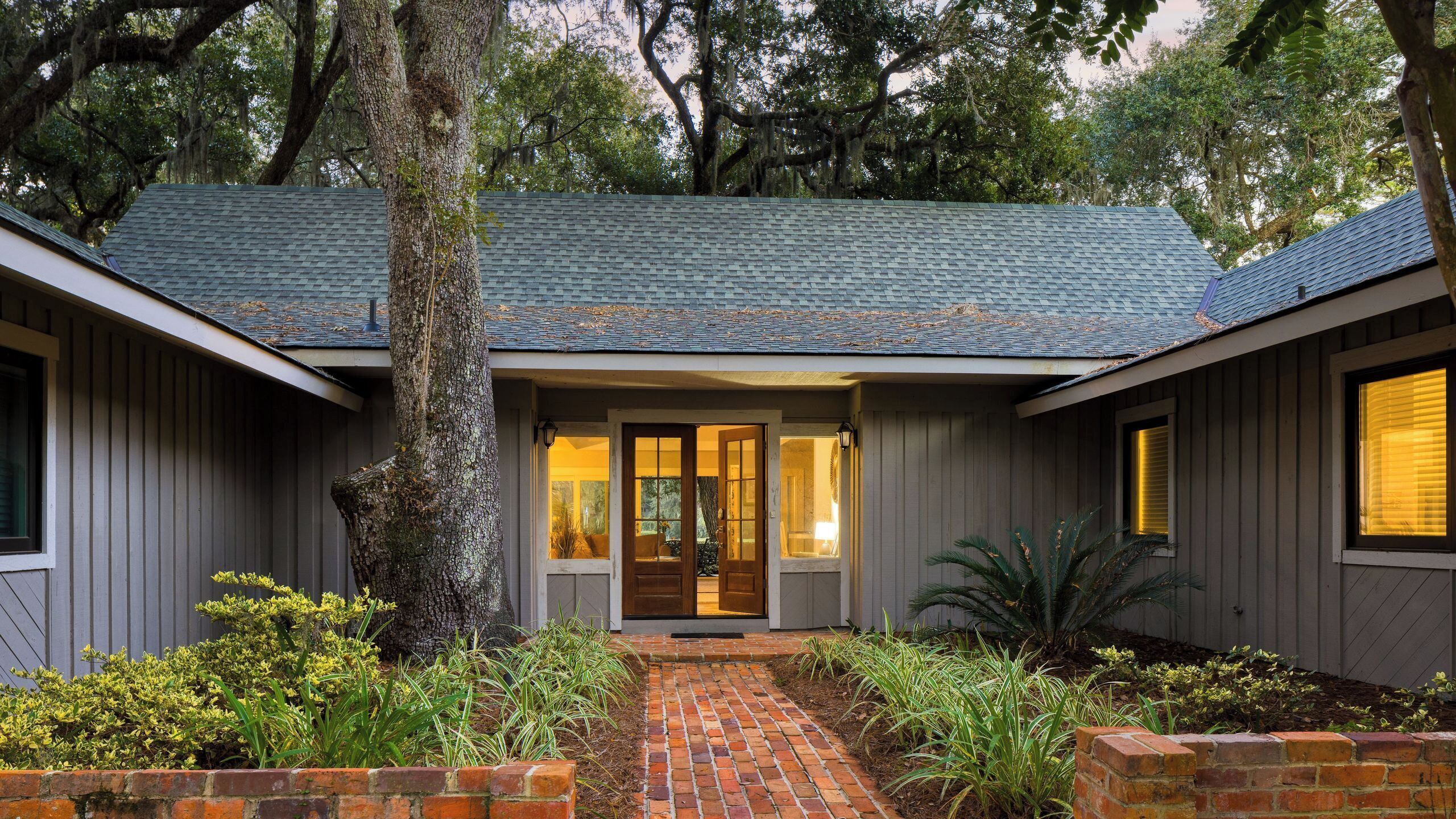 A two-story house with a brick pathway leading to the front door, surrounded by greenery and trees.