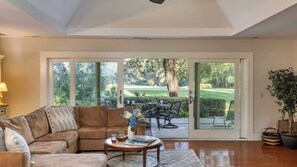 Amplio salón con un gran ventanal corredero que da a un patio con vistas a un campo de golf.