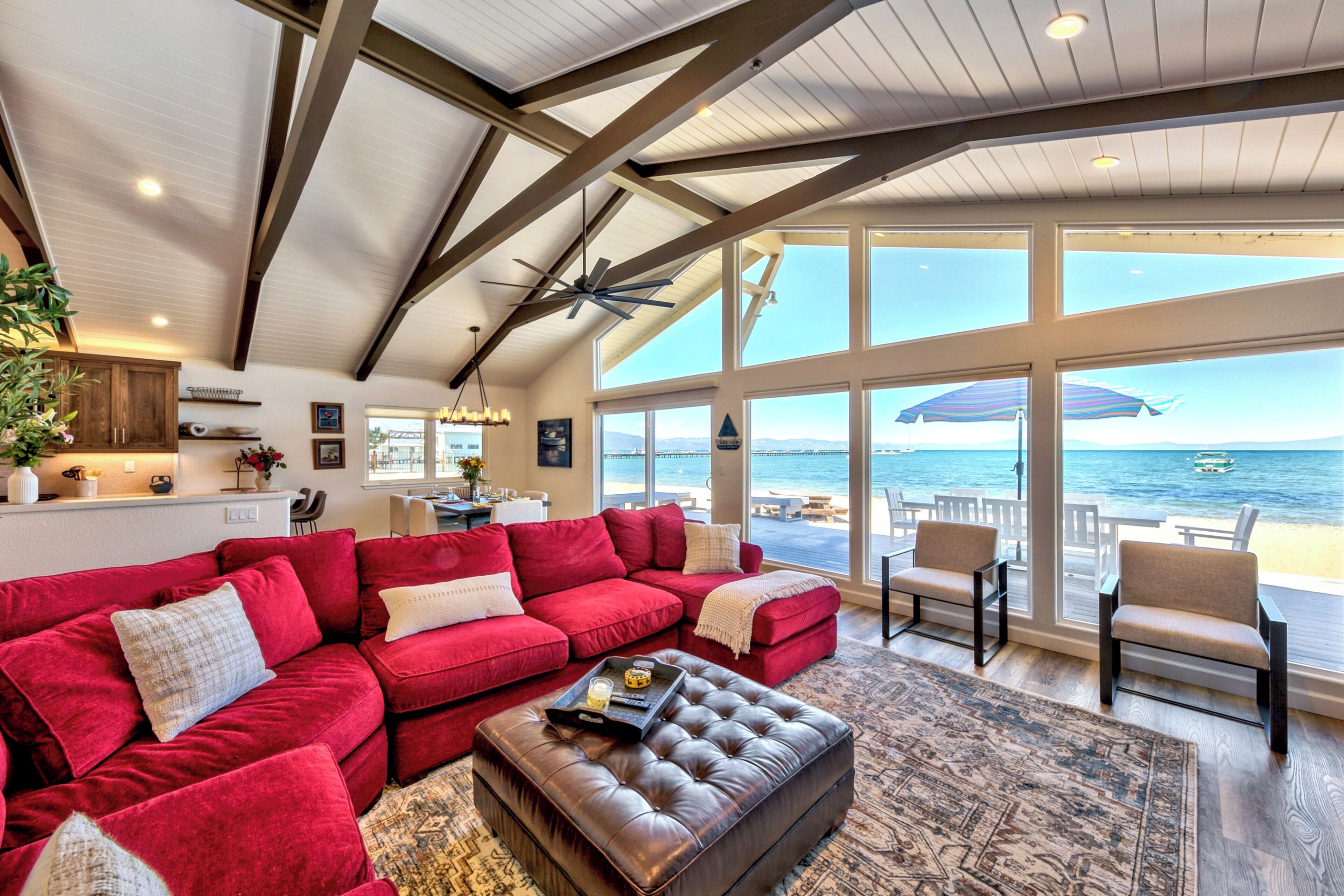 A spacious living room with a red sectional sofa, a leather ottoman, and a view of the ocean through large windows.