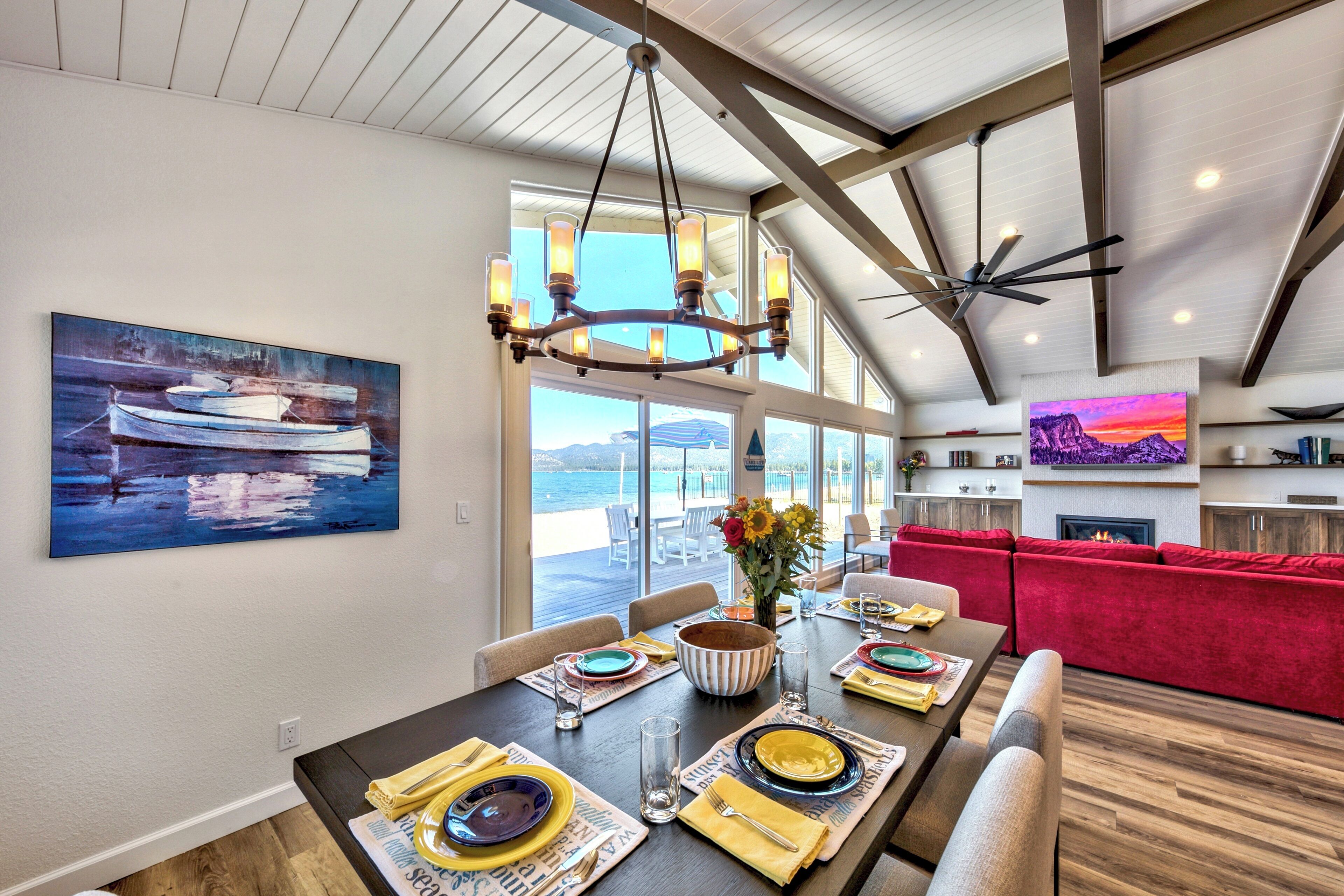 A dining area with a table set for four, a chandelier, and a painting of boats on the wall.