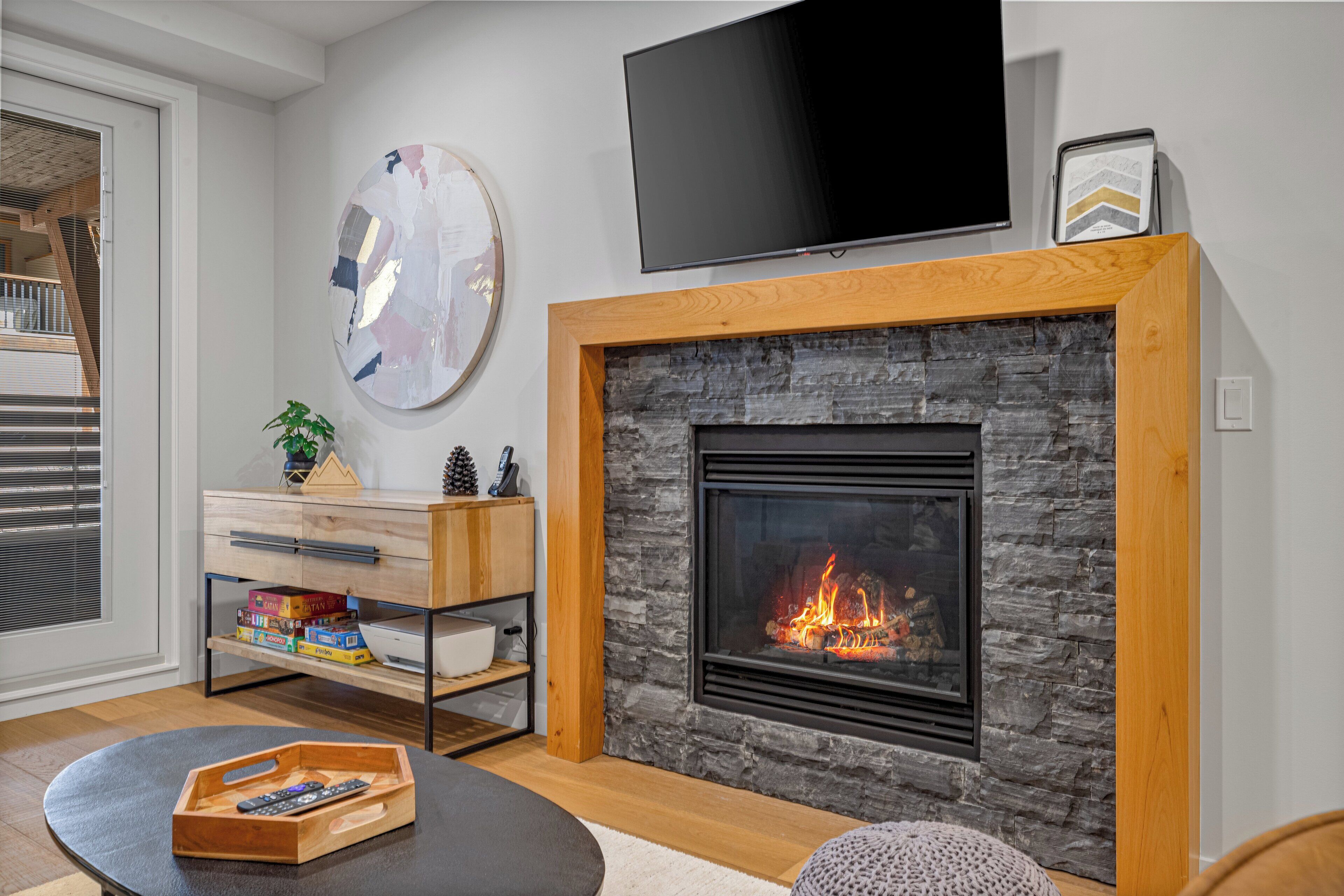 A living room with a stone fireplace, a flat-screen TV mounted above it, and a wooden entertainment unit with books and decorative items.