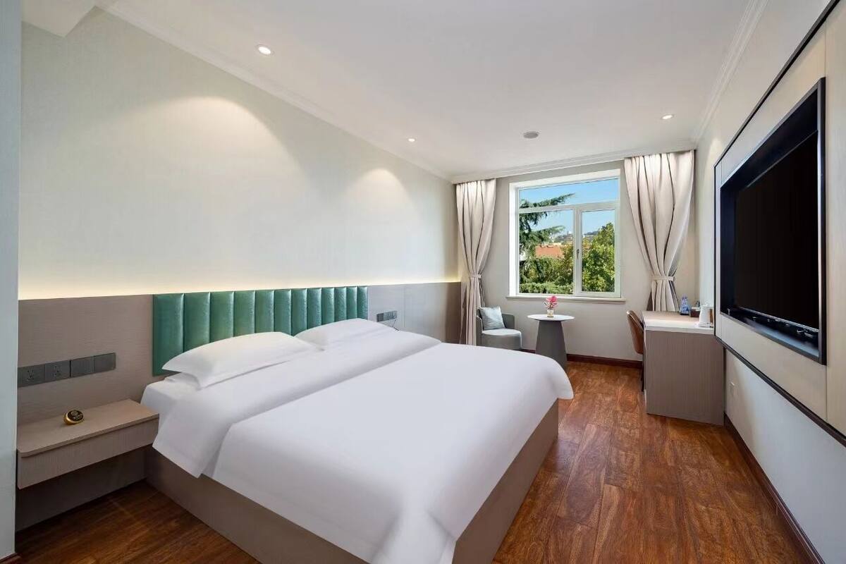 A hotel room with two beds, a TV, a desk, and a window with curtains.