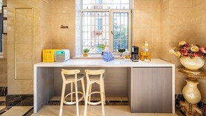 Un espace d’accueil d’hôtel avec un comptoir en marbre, deux tabourets de bar en bois, une machine à café, un flacon de gel hydroalcoolique et un vase rempli de fleurs.