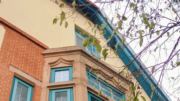 Un coin d’un bâtiment dont la façade est en briques, avec des encadrements de fenêtres bleus et des arrangements floraux décoratifs.