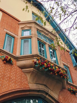 Eine Gebäudeecke mit Backsteinfassade, blauen Fensterrahmen und dekorativen Blumenarrangements.