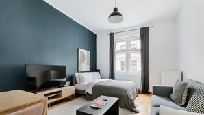 Moderni hotellihuone, jossa on sänky, työpöytä, televisio ja ikkuna, jossa on verhot.
