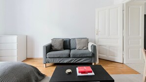 Moderni olohuone, jossa on harmaa sohva, kaksi kuviollista koristetyynyä, musta sohvapöytä, jonka päällä on kirja, ja valkoinen ovi.