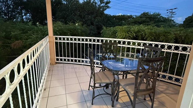 Un espacio al aire libre techado con una mesa y sillas, rodeado por una barandilla blanca.