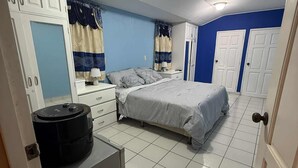 Un dormitorio con cama, un refrigerador pequeño, una mesita de noche y una lámpara en el techo.