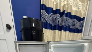 Un refrigerador abierto con dispensador de agua, un estante con latas rojas y una puerta con cortina azul y blanca.