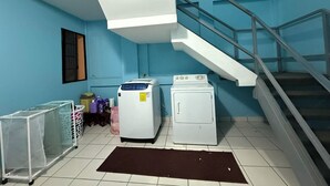 Un lavadero con dos lavadoras, una secadora, una escalera metálica y un carrito con bolsas de ropa.