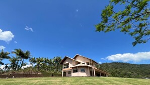 Una casa de dos pisos con un amplio jardín delantero y palmeras al fondo.