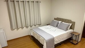 Un dormitorio con cama, mesita de noche, ventana con cortinas y suelo de madera.