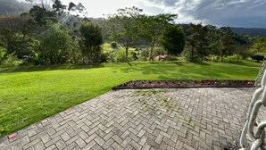 Un área de patio pavimentada con un diseño de ladrillo, rodeada de césped cuidado y varios árboles.