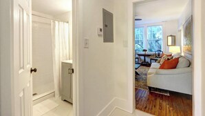 A hallway leading to a living room with a white couch, a small table, and a window with a view of trees. - Luxury Stay in a Restored 1920s Savannah Home (Savannah)