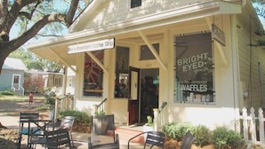 A small, single-story building with a porch, a sign for a breakfast and coffee shop, and a large window advertising waffles. - Vibe at The Porter (Ocean Springs)